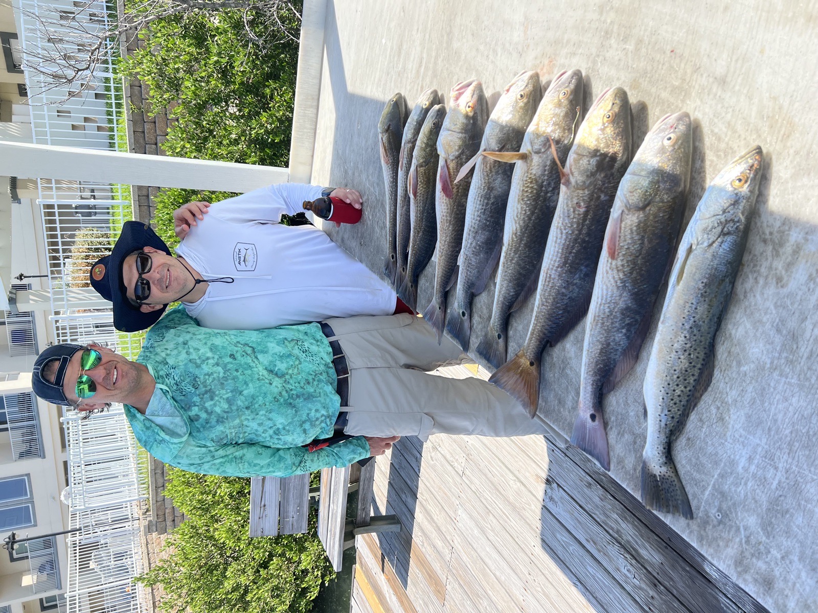 Two anglers on the dock with a row of speckled trout